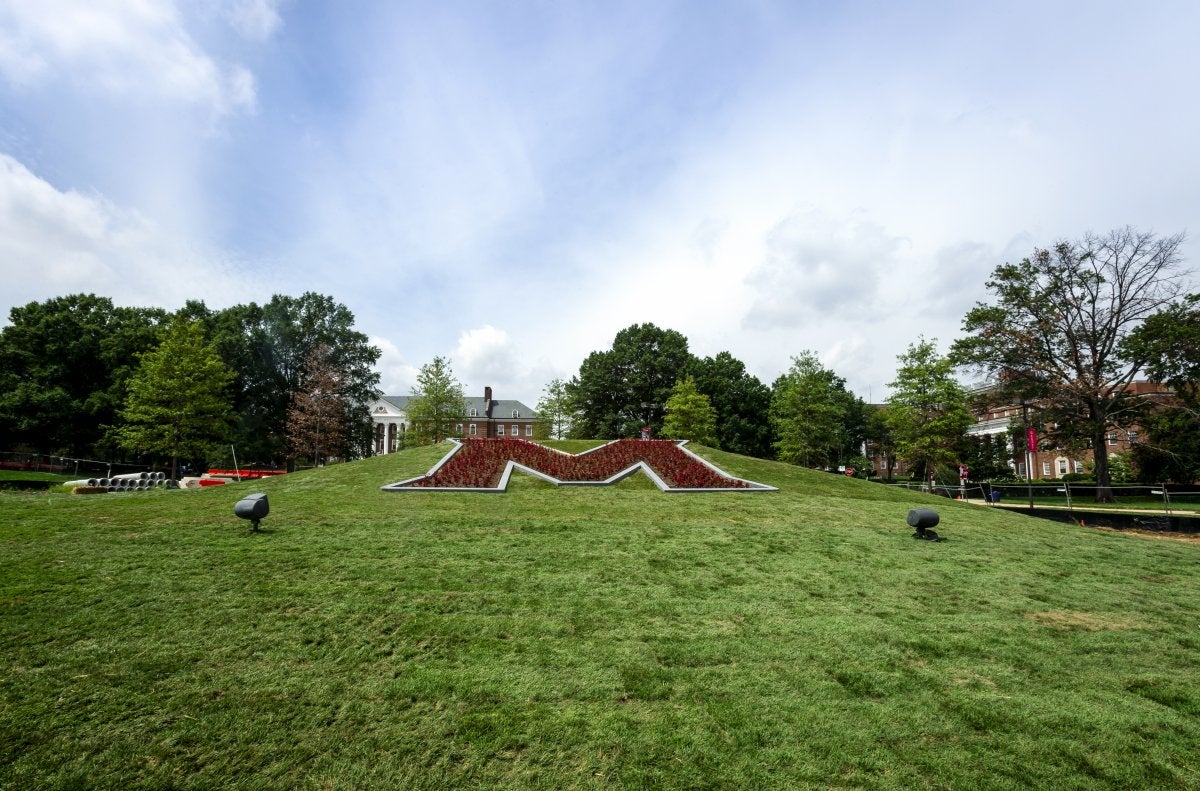 New M placement on UMD lawn. Large M on a grassy hill surrounded by flowers.