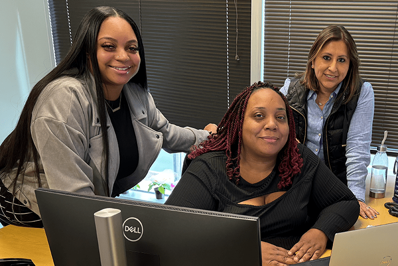 Three staff members at a desk with a computer